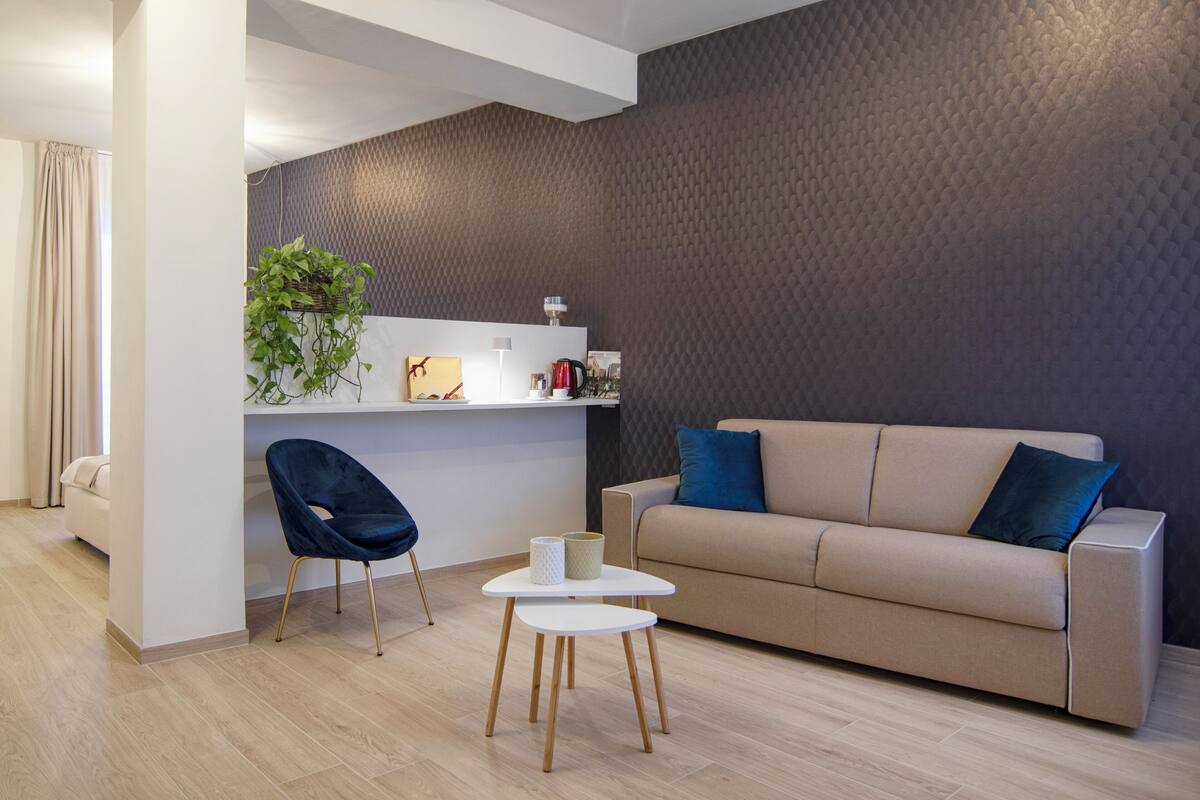 Ein modernes Wohnzimmer mit einem beigen Sofa, einem dunkelblauen Sessel und einem kleinen weißen Tisch.
