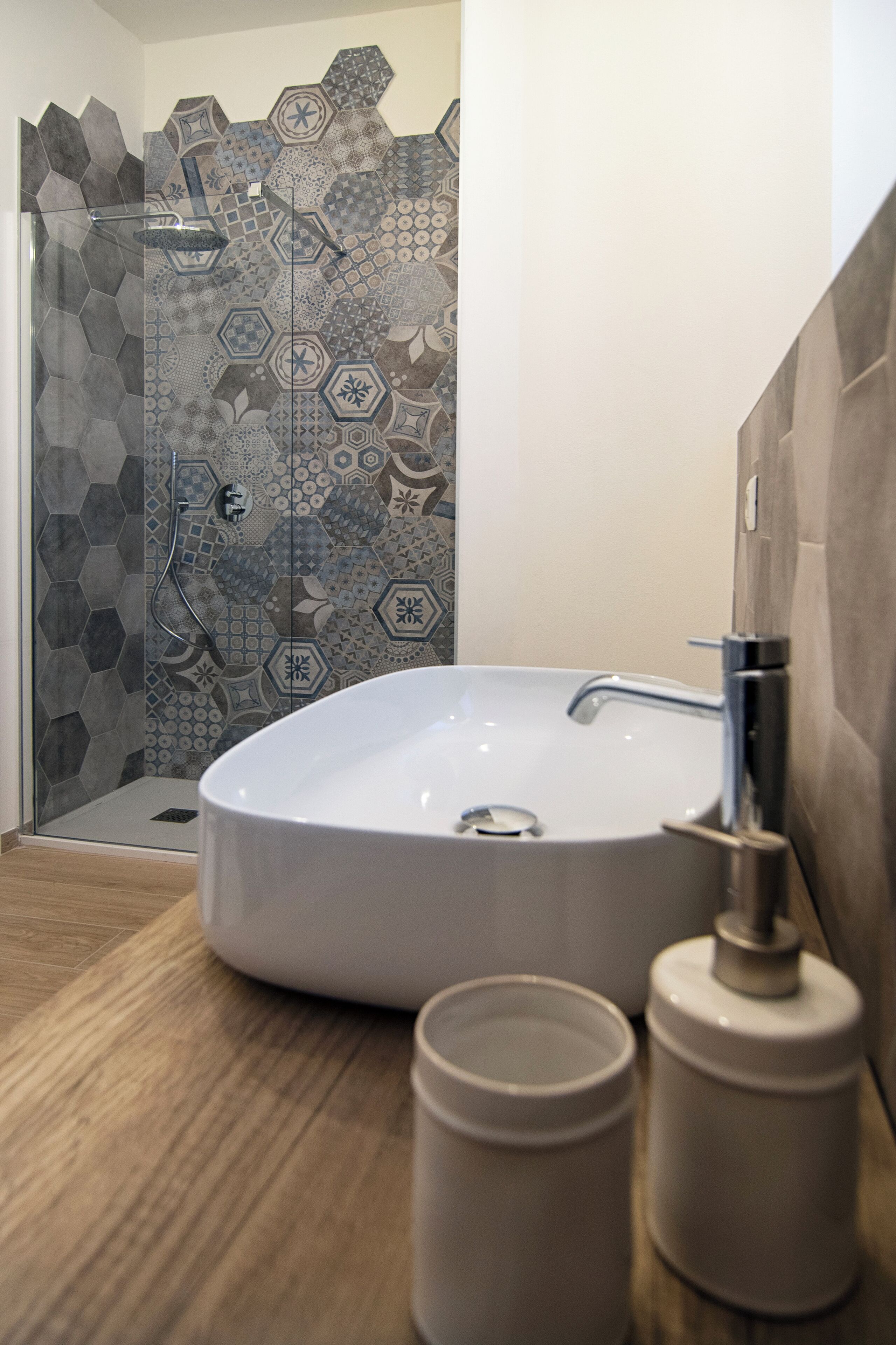 A bathroom with a large white sink, a shower with a glass door, and a tiled wall with geometric patterns.