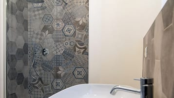 Un baño con un lavamanos grande de color blanco, una ducha con puerta de vidrio y una pared de azulejos con diseños geométricos.