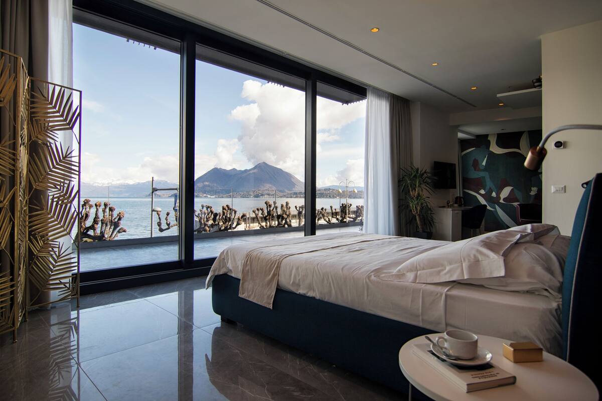 Ein modernes Schlafzimmer mit einem großen Bett, Blick auf Meer und Berge sowie minimalistischer Einrichtung.