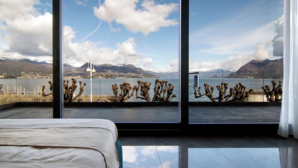 Quarto com uma grande janela com vista para um lago e montanhas.