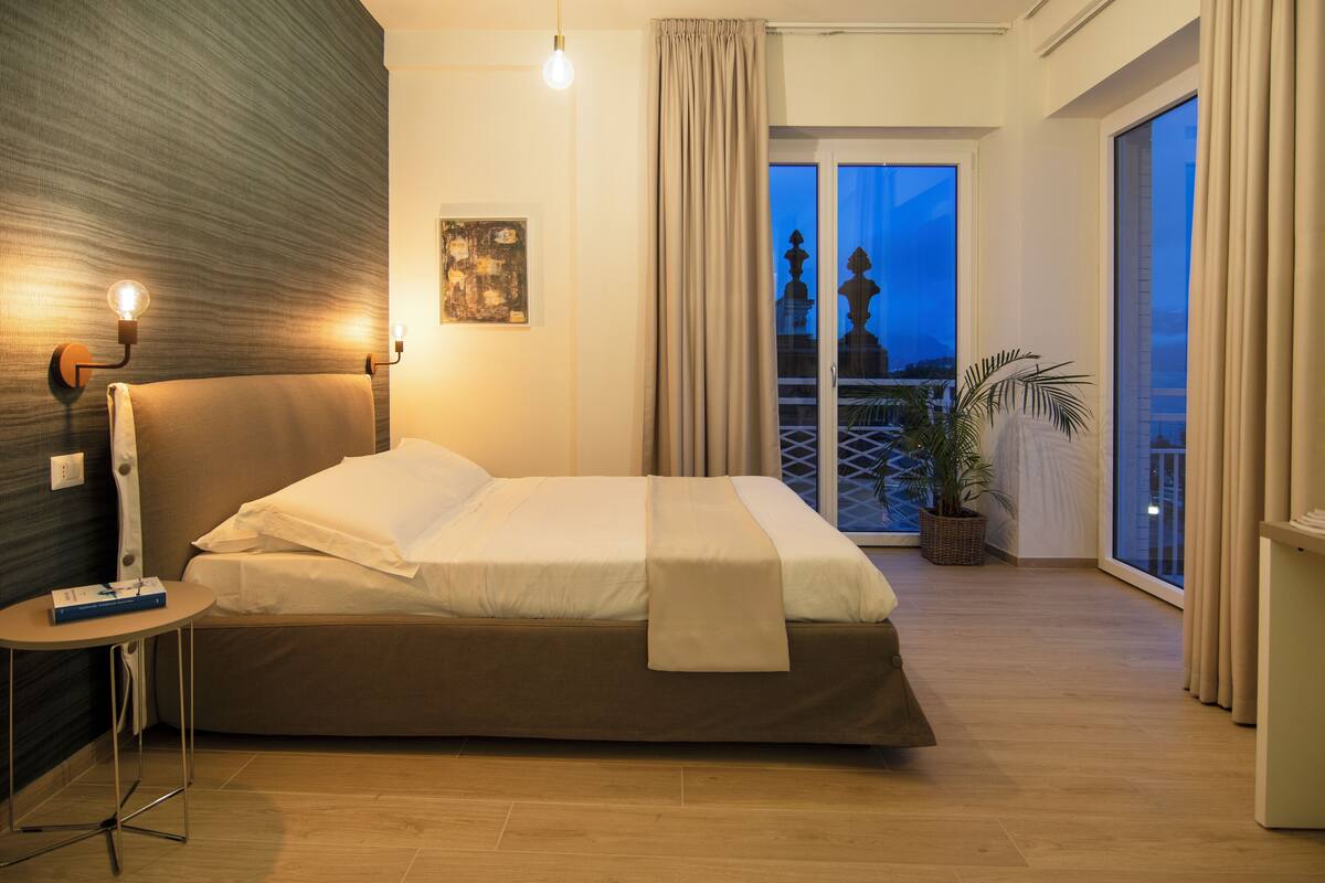 Ein gut beleuchtetes Schlafzimmer mit einem Bett, einem Nachttisch und Blick ins Freie.