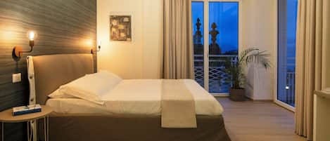 A well-lit bedroom with a bed, bedside table, and a view of the outside.