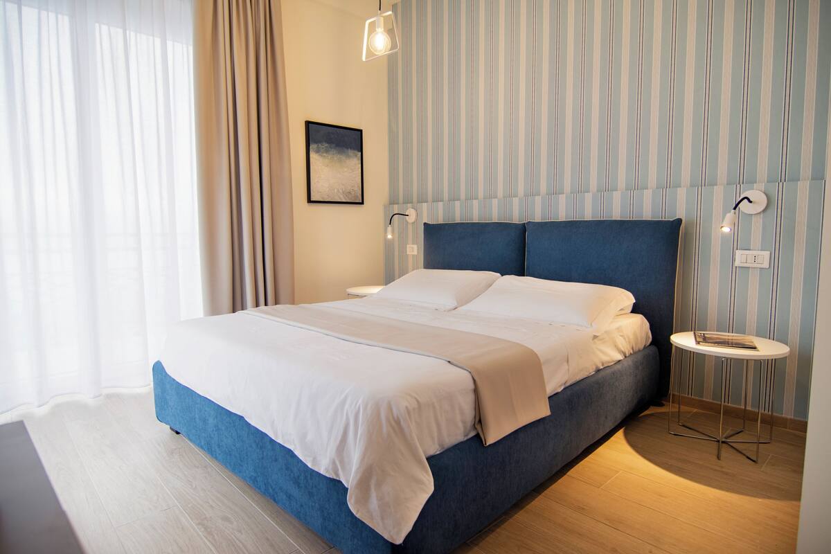 Ein modernes Schlafzimmer mit einem großen Bett, einem Nachttisch und einer wandmontierten Lampe.