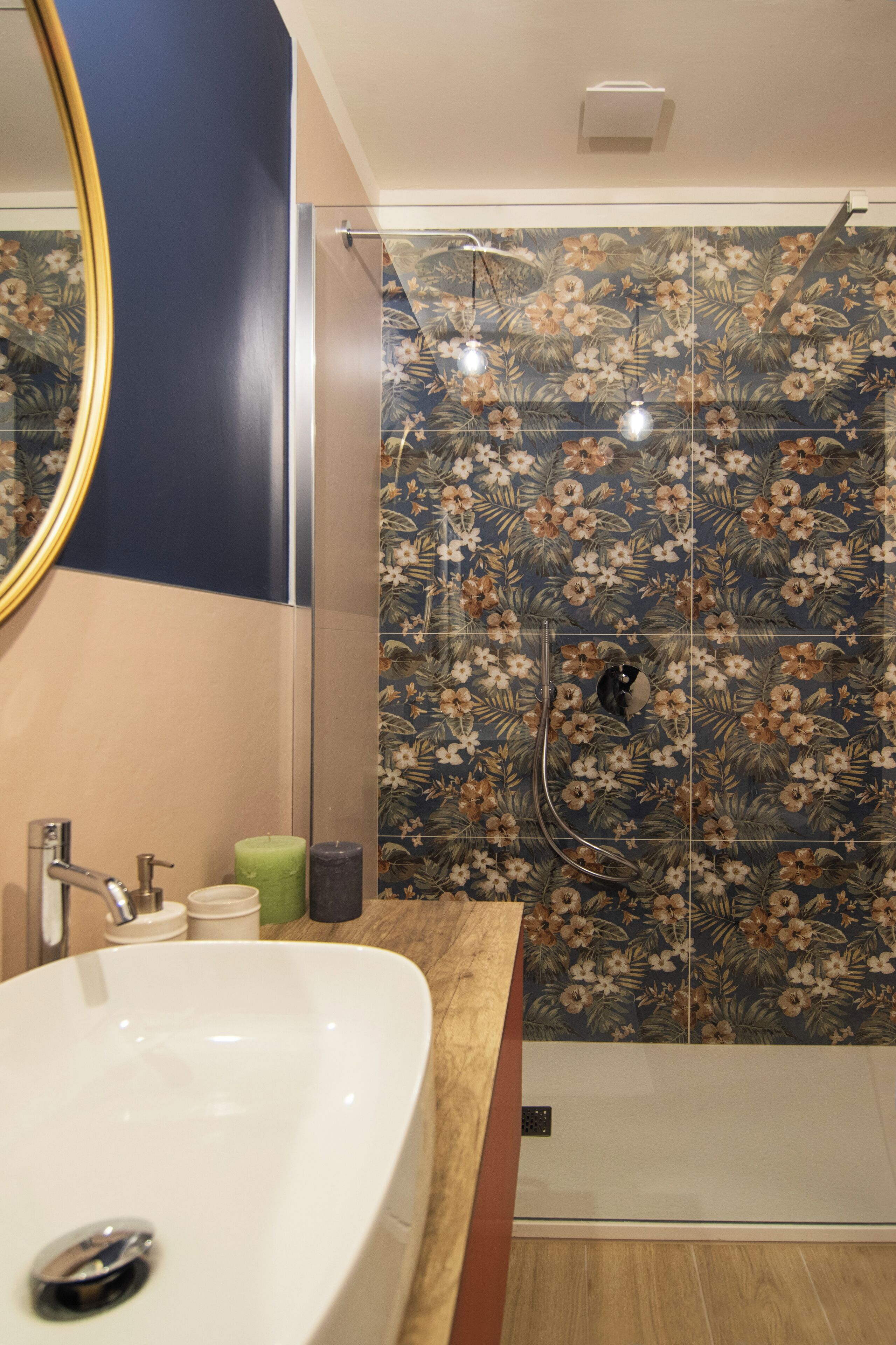 Une salle de bain avec un lavabo blanc, un miroir et une douche aux carreaux à motifs floraux.