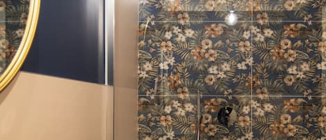 A bathroom with a white sink, a mirror, and a shower with floral tiles.
