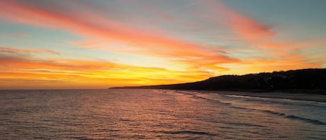 A coastal sunset with a calm sea and a distant shoreline.
