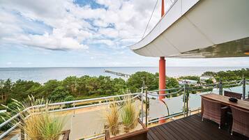 Eine Terrasse mit Blick aufs Meer, einem Holztisch und Korbstühlen.