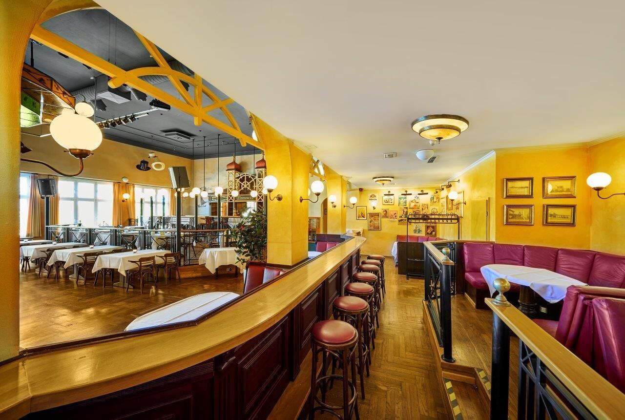 Een restaurant met een bar, zitplaatsen in hokjes en hoge plafonds met zichtbare balken.