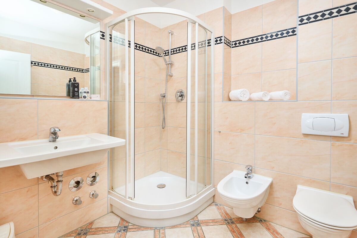 A modern bathroom with a glass-enclosed shower, a pedestal sink, a bidet, and a toilet.