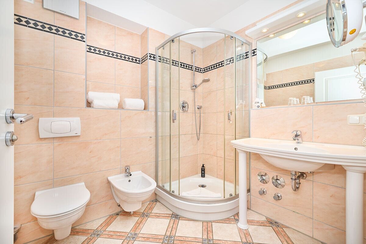 A modern bathroom with a glass-enclosed shower, a pedestal sink, a toilet, and a bidet.