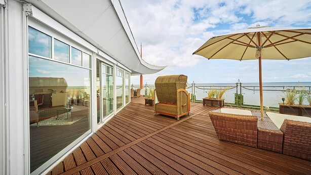 A deck with wicker furniture and a large umbrella, overlooking the sea. - Strandhotel Prinz von Preussen (Zinnowitz)