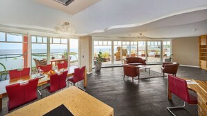 A spacious room with a large dining table, red chairs, and a view of the ocean through large windows. - Strandhotel Prinz von Preussen (Zinnowitz)