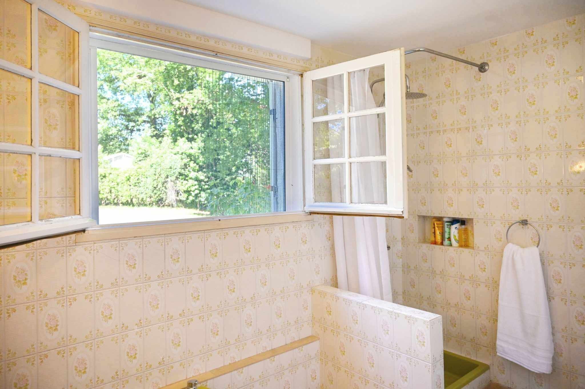 A bathroom with a window, shower, and tiled walls.