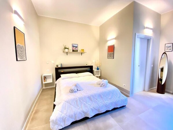 A modern bedroom with a large bed, bedside tables, and wall-mounted shelves.