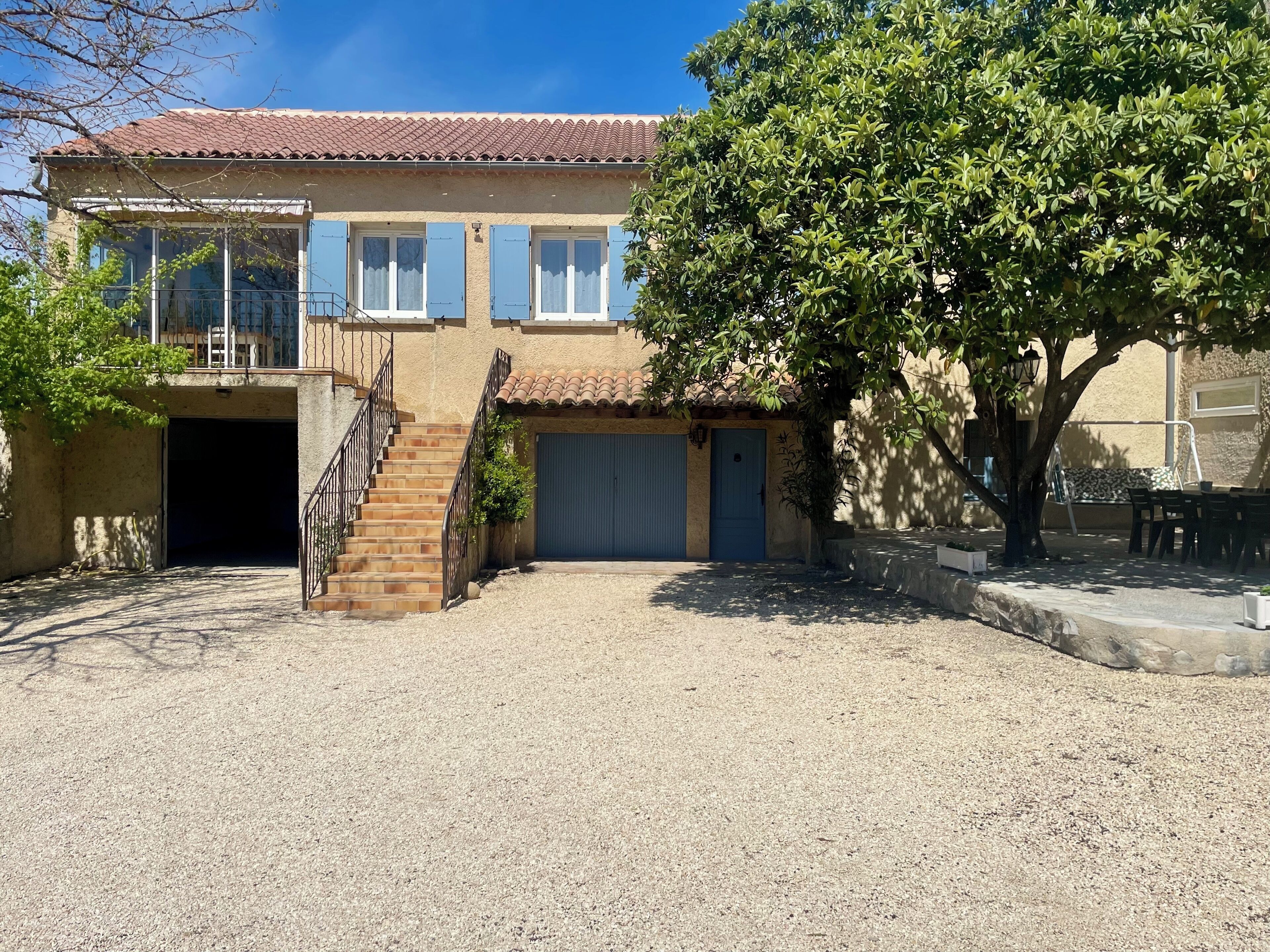 A two-story house with a tiled roof, a covered driveway, and a tree in the foreground.