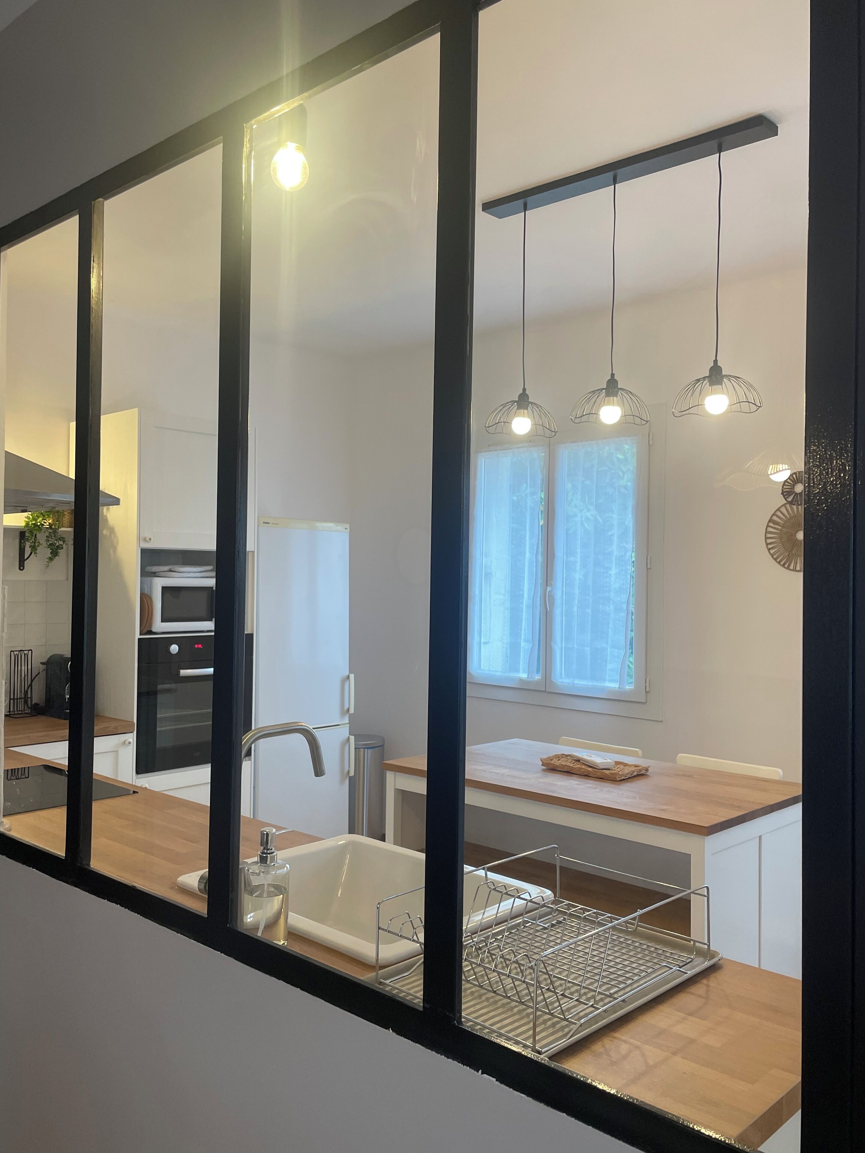 A modern kitchen with a large mirror, a sink, a microwave, and a stove. There are hanging pendant lights above the counter.