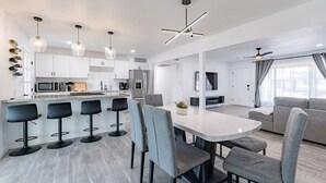 A modern kitchen with white cabinets, a central island with bar stools, and a dining area with grey chairs. - Scottsdale Lux Oasis, Pool Hot Tub Sleeps 12! (Scottsdale)