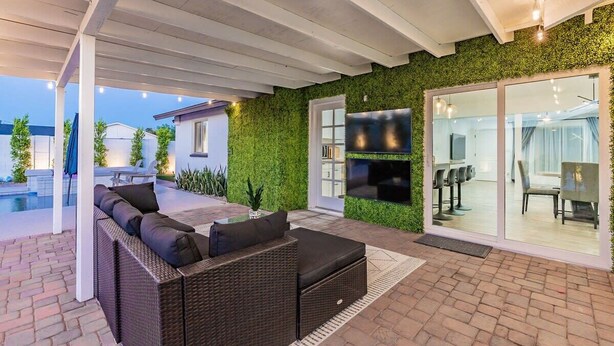 A covered outdoor seating area with a wicker sofa and a glass door leading to a dining area. - Scottsdale Lux Oasis, Pool Hot Tub Sleeps 12! (Scottsdale)