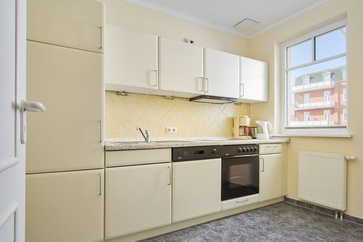 A kitchen with white cabinets, a stove, and a window with a view of buildings.