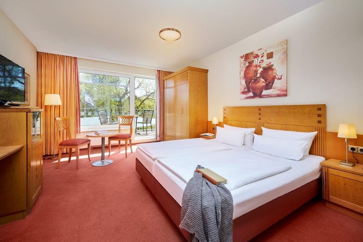 A hotel room with a large bed, a desk, a chair, a TV, and a window with curtains.