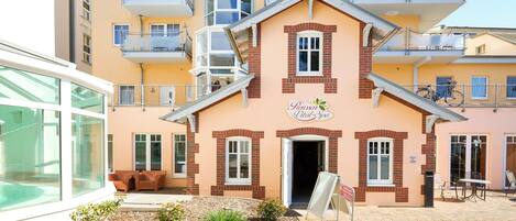 A multi-story building with balconies, a central entrance, and a small outdoor seating area.