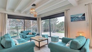 Un salon spacieux avec des canapés de couleur turquoise, une table basse et de grandes fenêtres donnant sur l’extérieur.