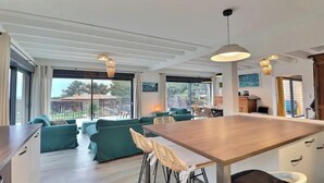 Une cuisine moderne avec un îlot central en bois, des canapés verts et des chaises en osier.