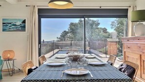 Un coin repas avec une table dressée pour quatre personnes, une chaise en osier, un buffet et un tableau accroché au mur.