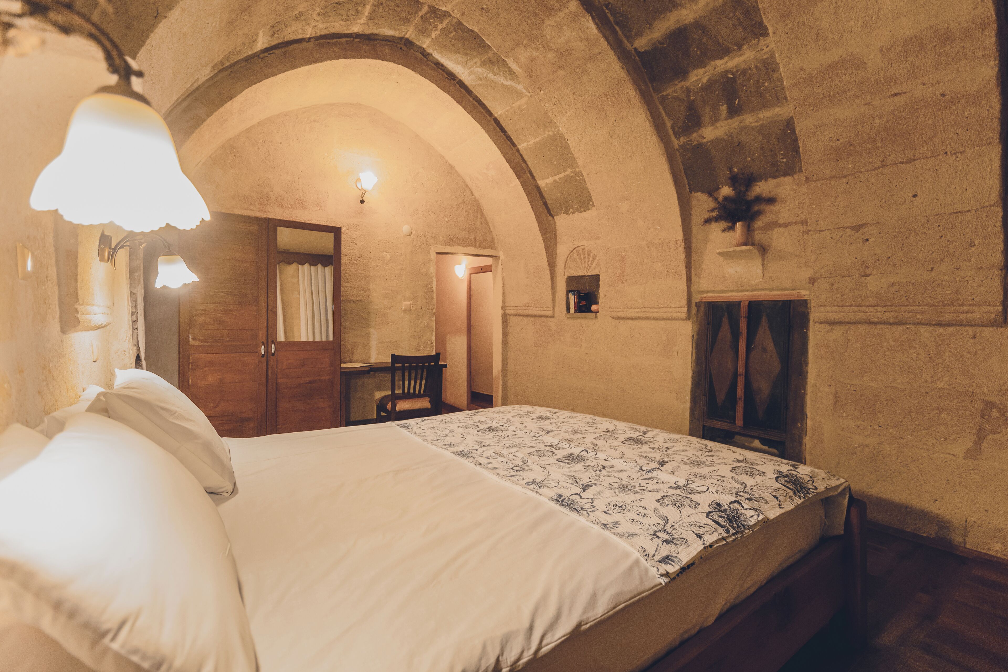 A bedroom with a bed, a desk, and an arched stone ceiling.