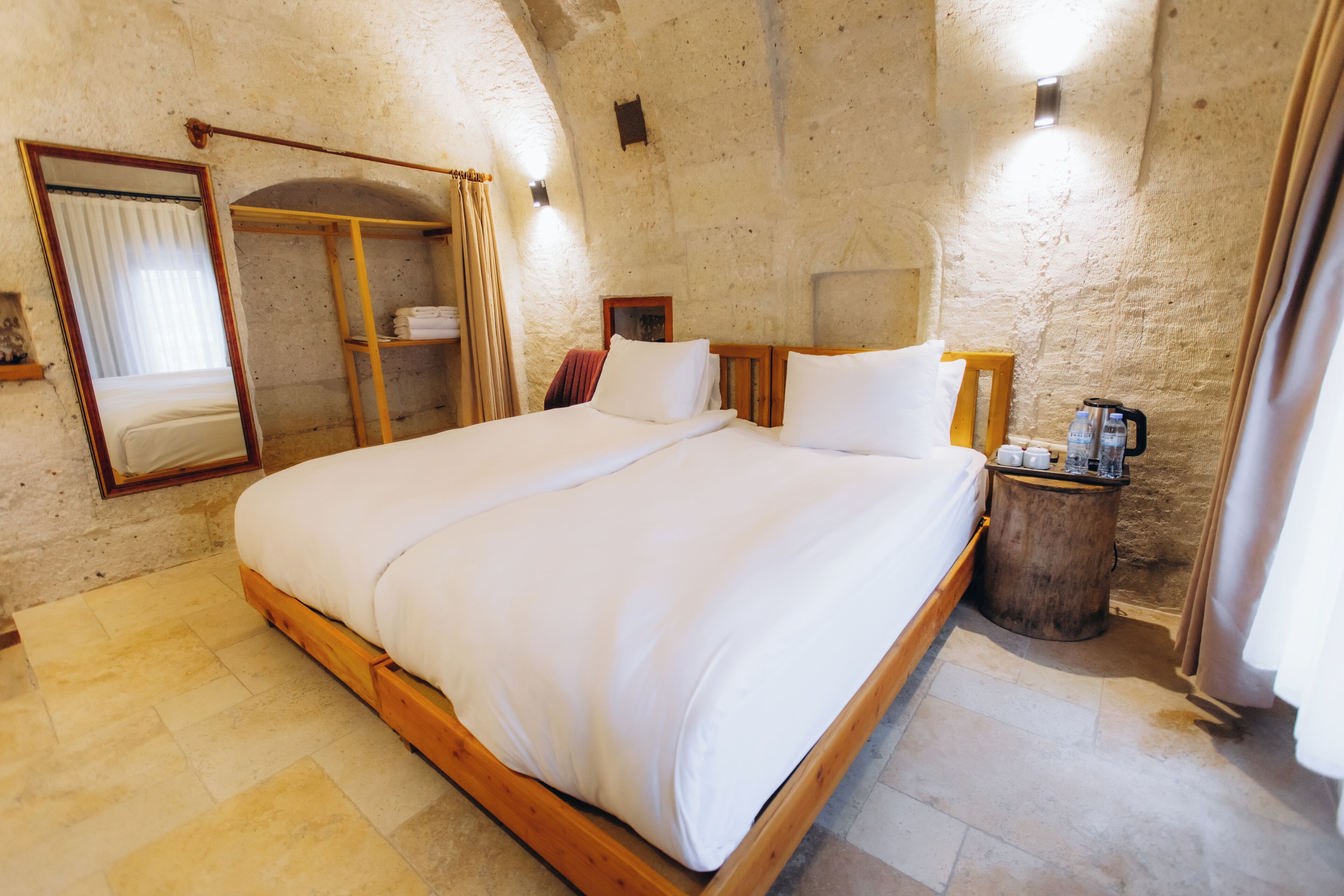 A bedroom with a large bed, a wooden headboard, a bedside table with a lamp, a mirror, and a wardrobe.