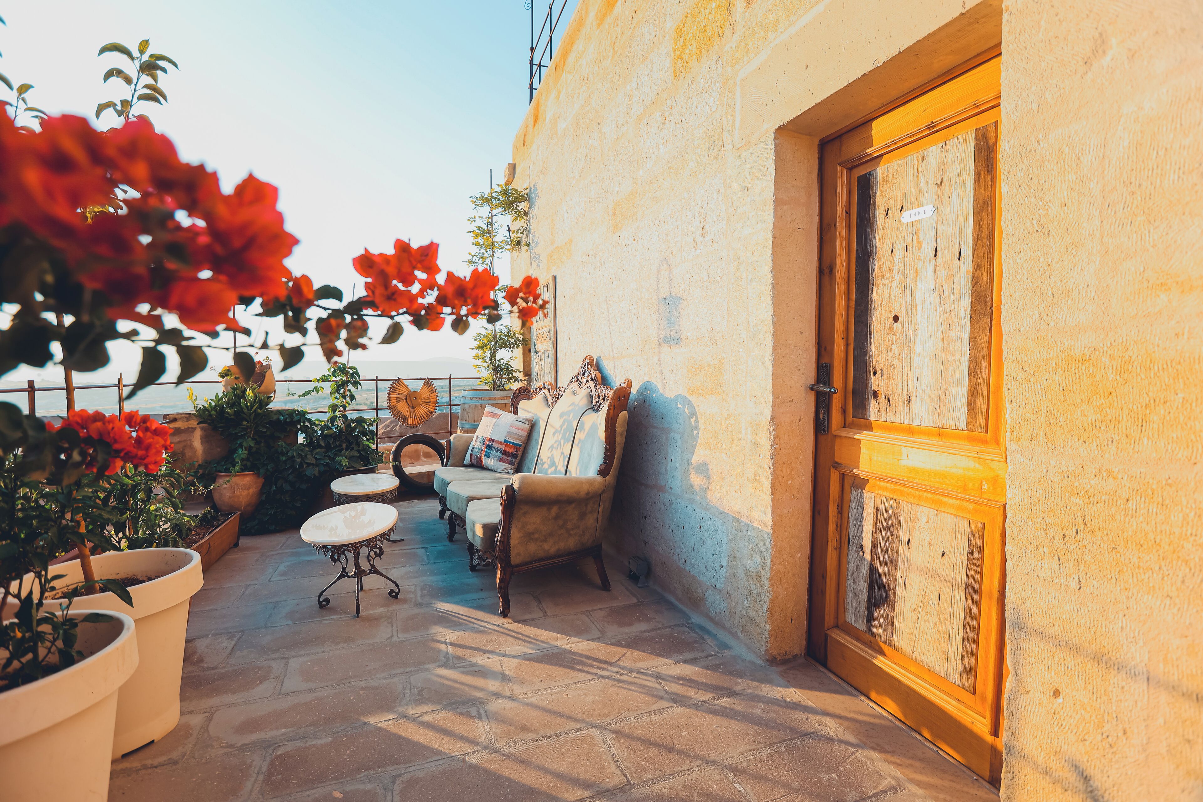 A patio with a wooden door, potted plants, a cushioned seating area, and a view of the sea.