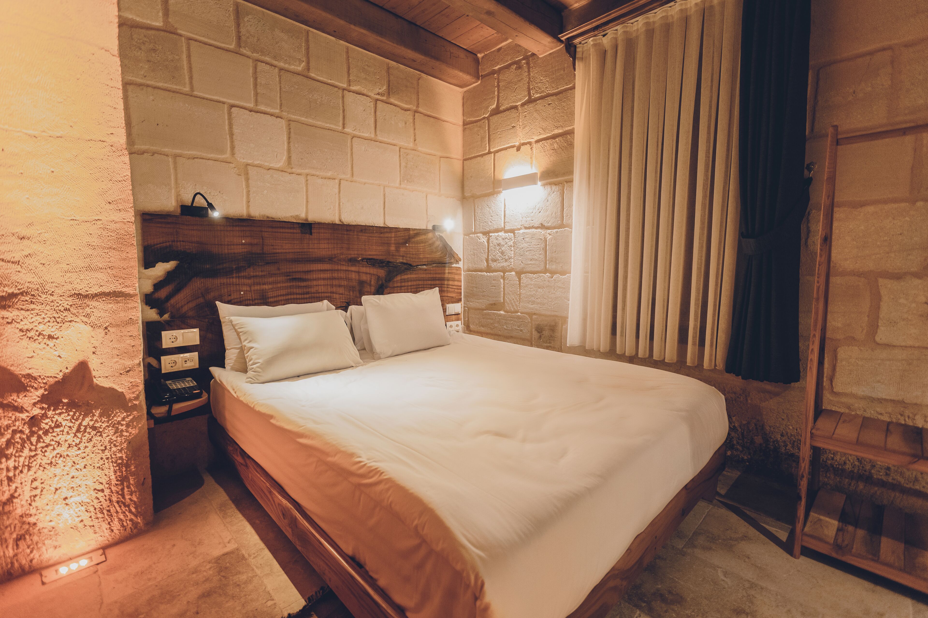 A bedroom with a wooden headboard, a bed with white bedding, a nightstand, and a wall-mounted light fixture.