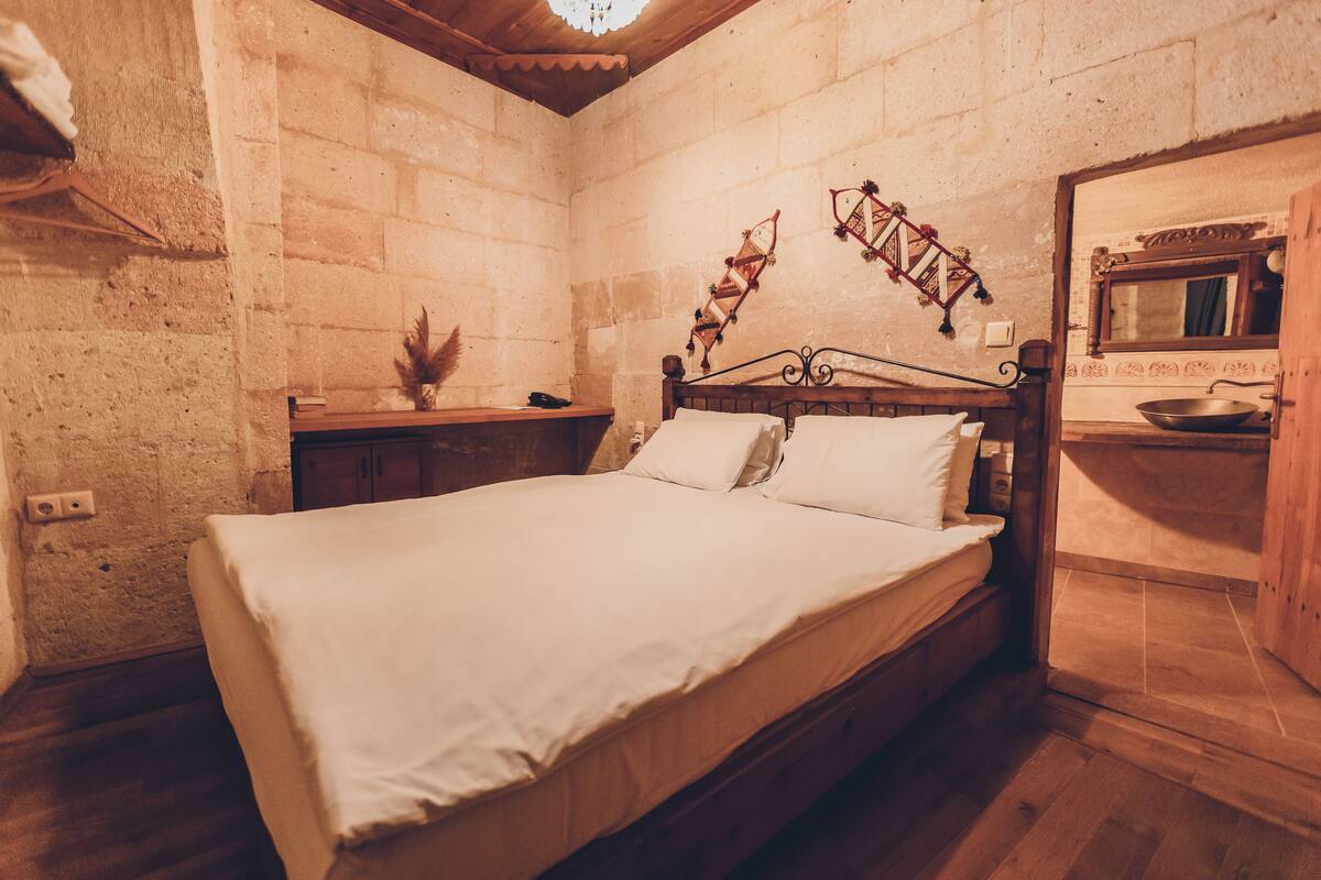 A bedroom with a wooden bed, a nightstand, a wall-mounted shelf, and a rustic brick wall.