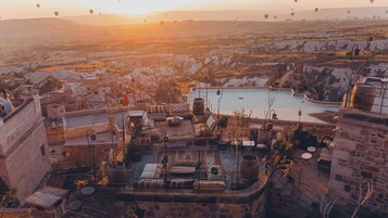 Terraza en la azotea con muros de piedra, una piscina y vistas a un valle con globos aerostáticos.