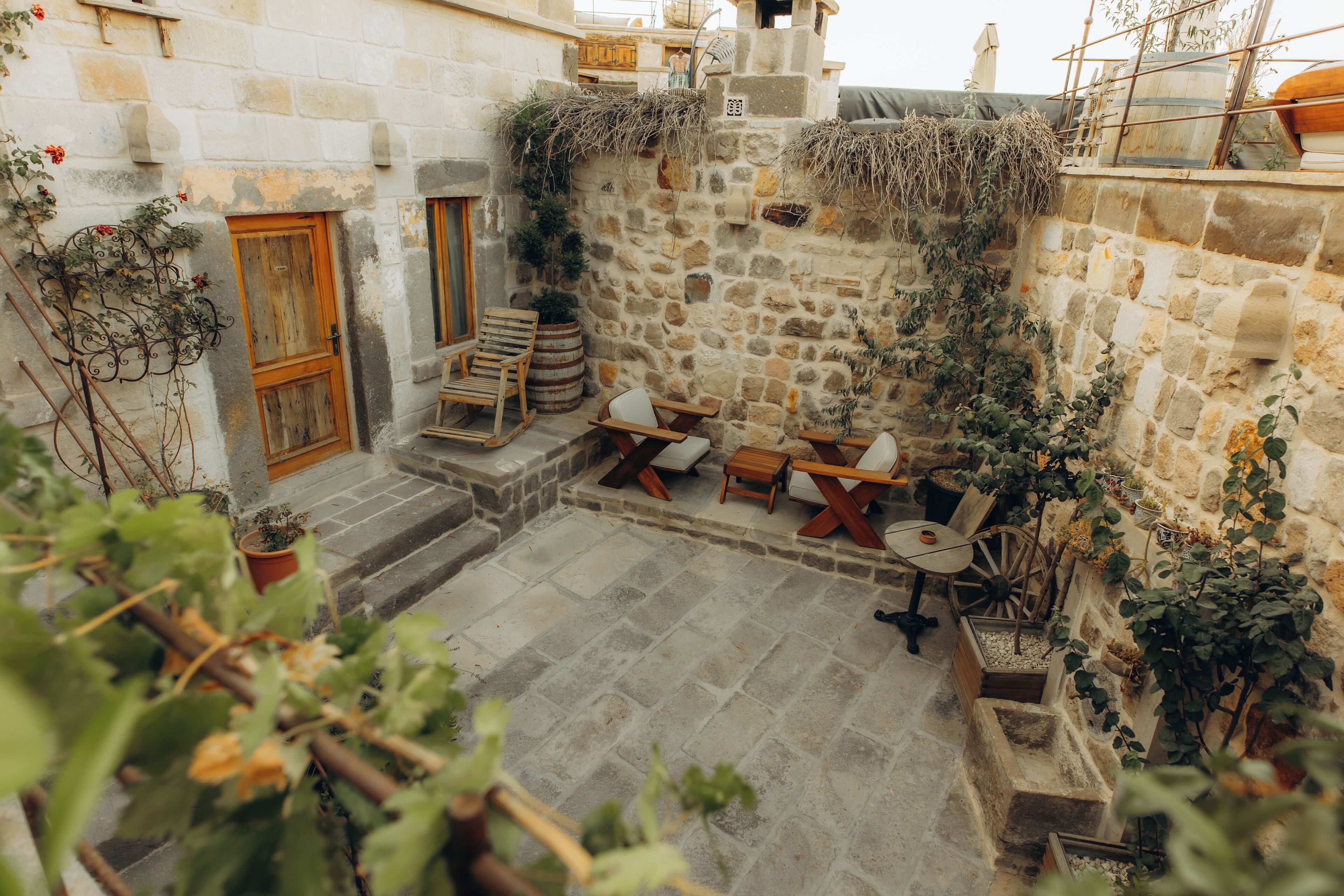 Un patio de piedra con muebles rústicos, plantas en macetas y una puerta de madera.