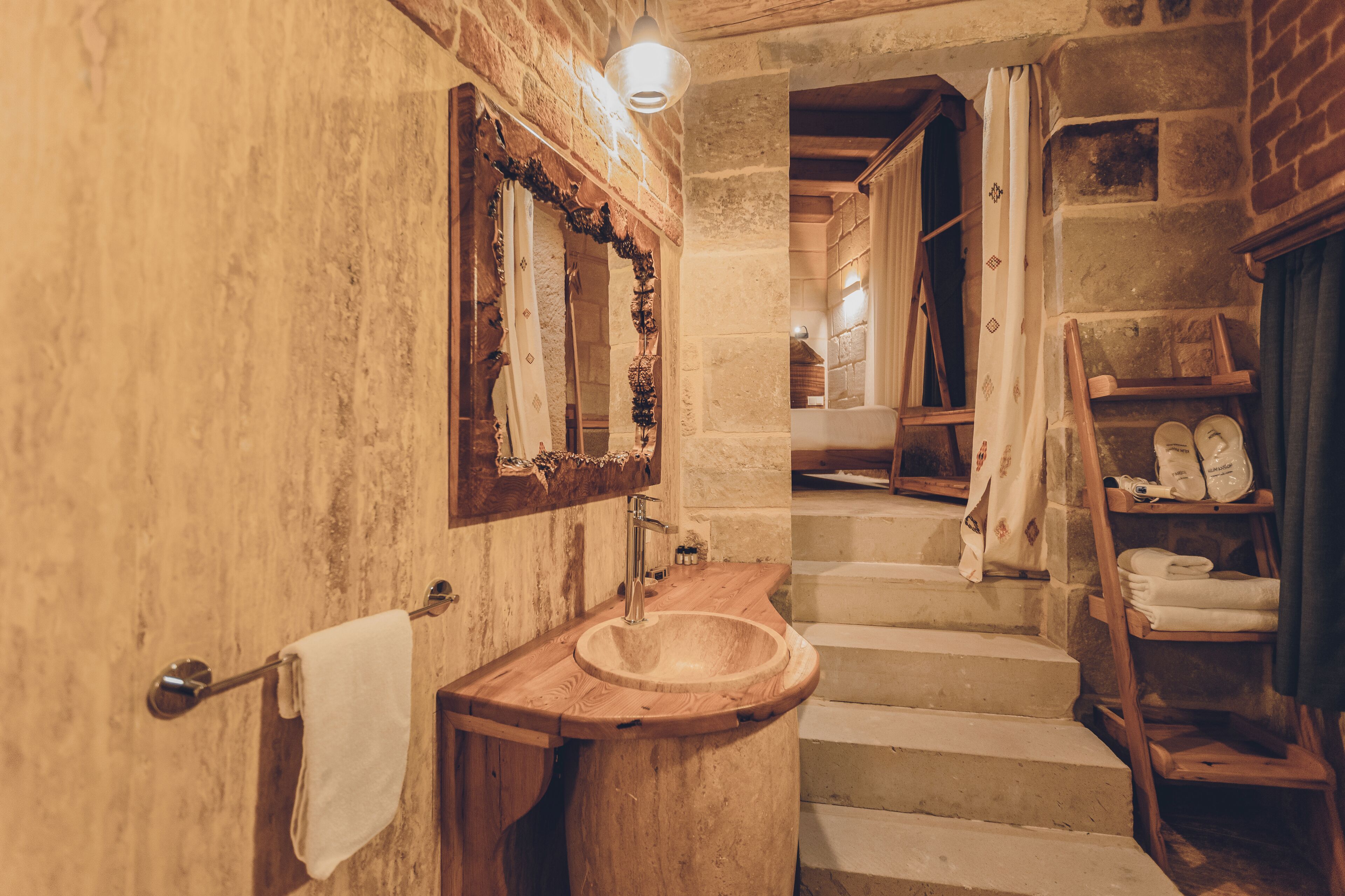 A rustic bathroom with a wooden sink, a mirror, and a staircase leading to another room.