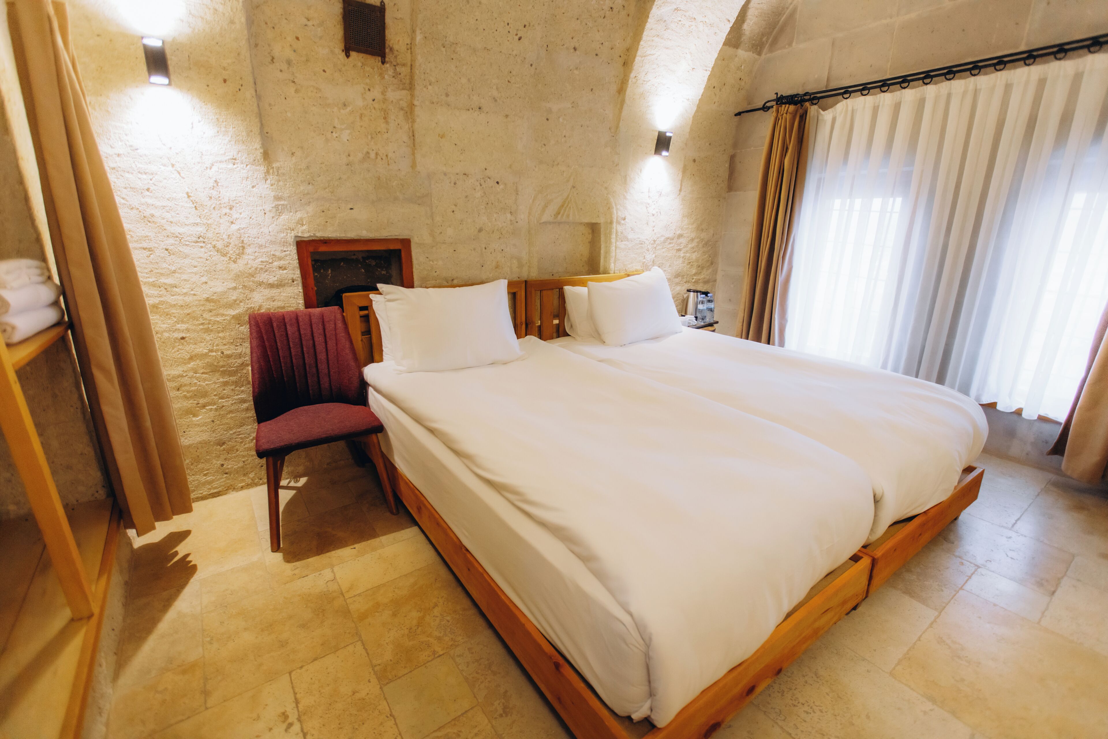 A bedroom with a large bed, a chair, a nightstand, and a wall-mounted lamp.