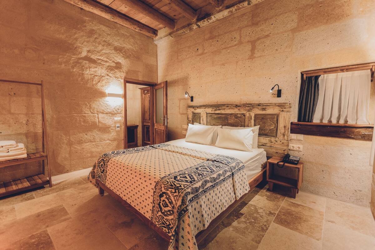 A bedroom with a wooden bed, a nightstand, a wall-mounted lamp, and a window with curtains.