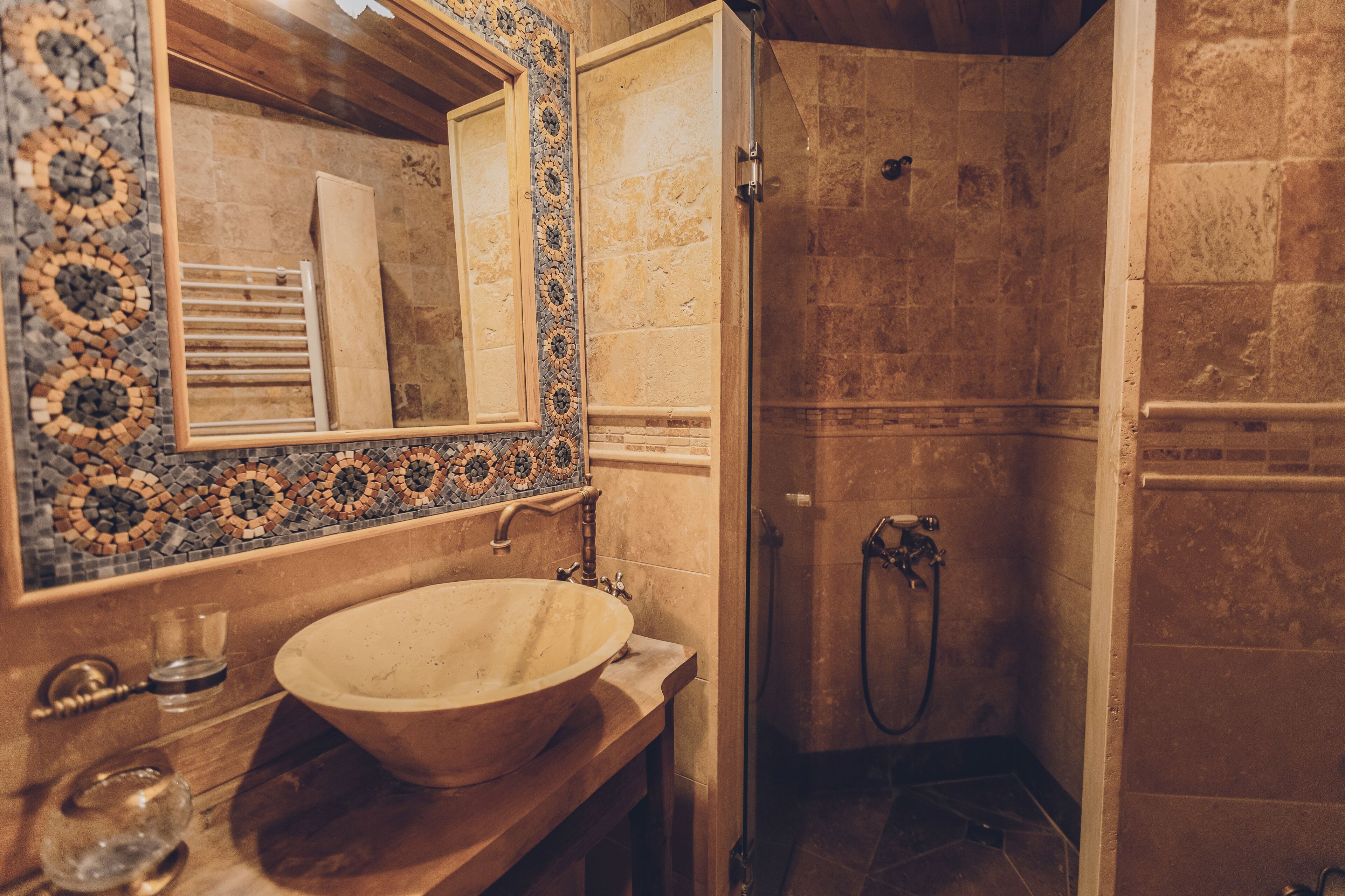 A bathroom with a large, round sink, a mirror with a mosaic border, and a shower area with stone tiles.