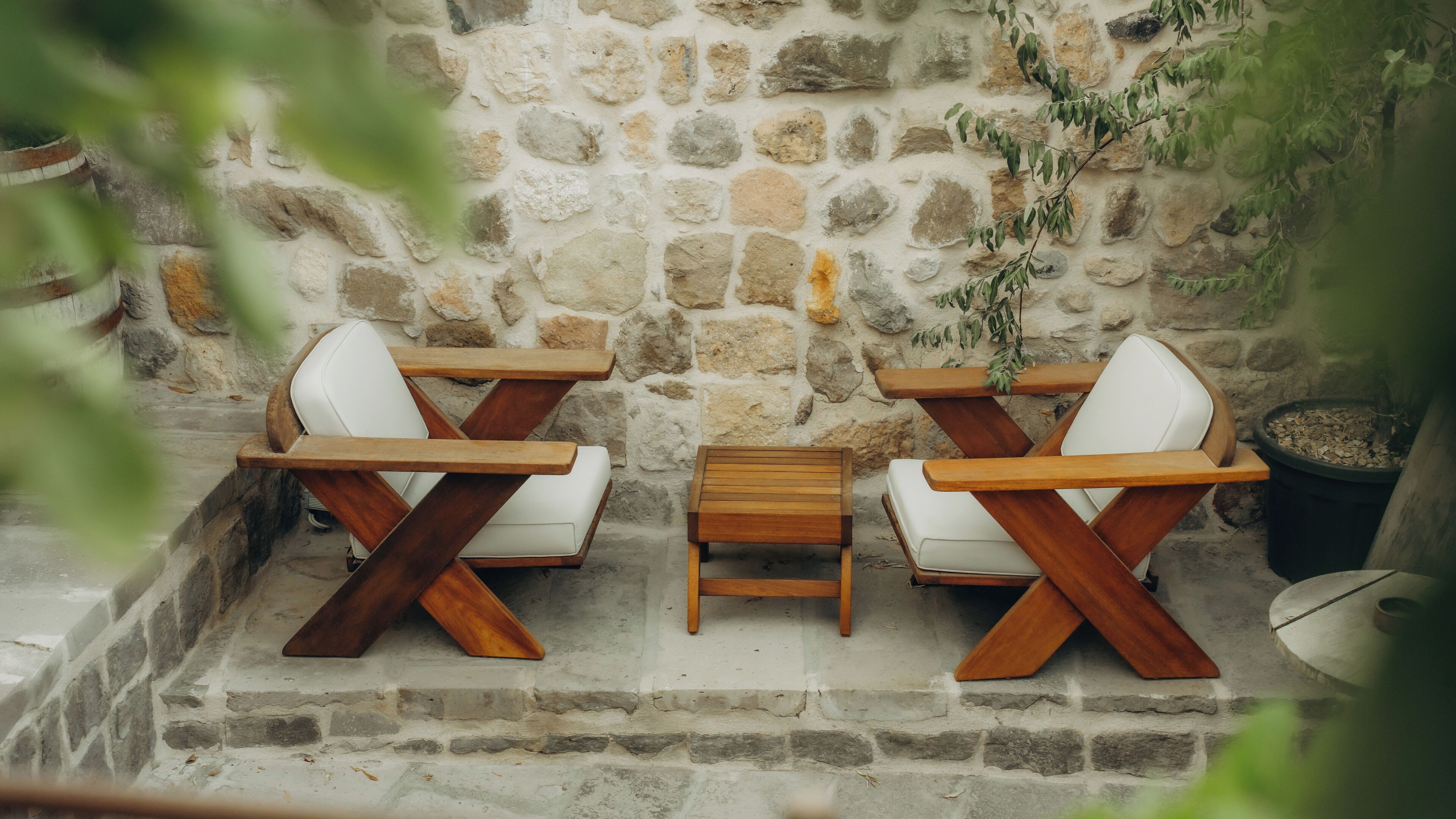 A stone wall with two wooden tables and white chairs.