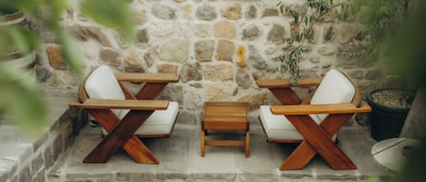 A stone wall with two wooden tables and white chairs.