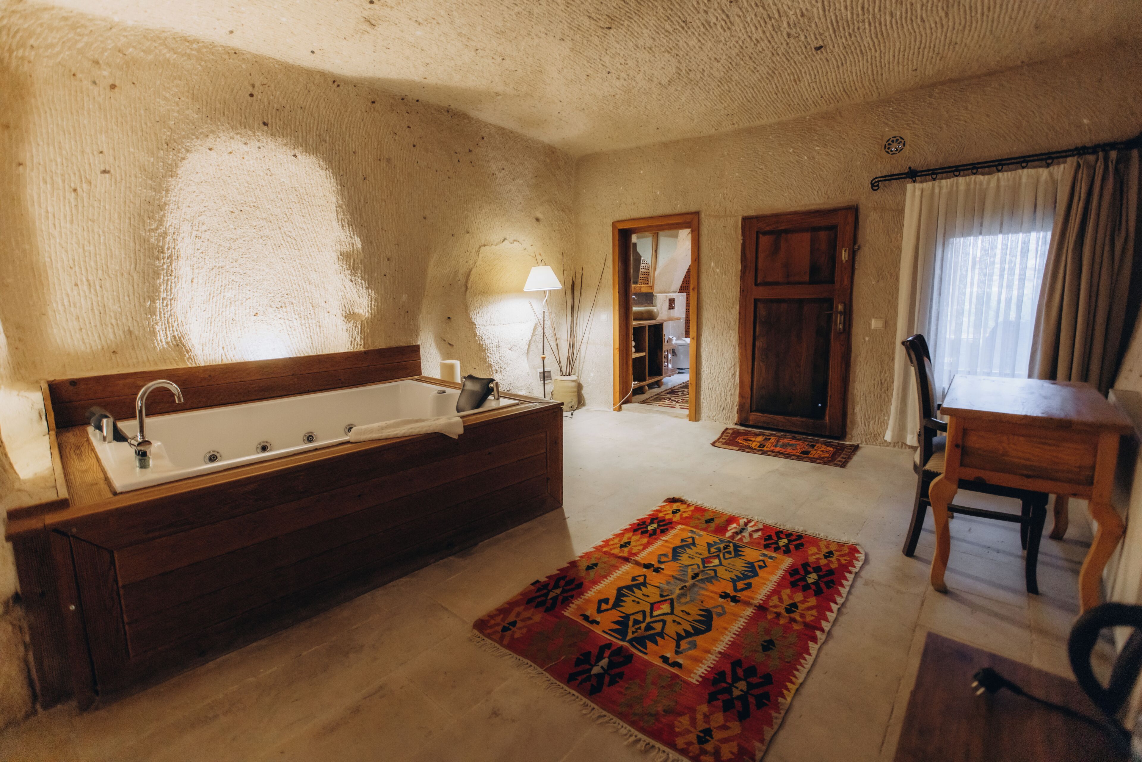 Une pièce avec une baignoire en bois, une chaise en bois, un tapis à motifs et un miroir.