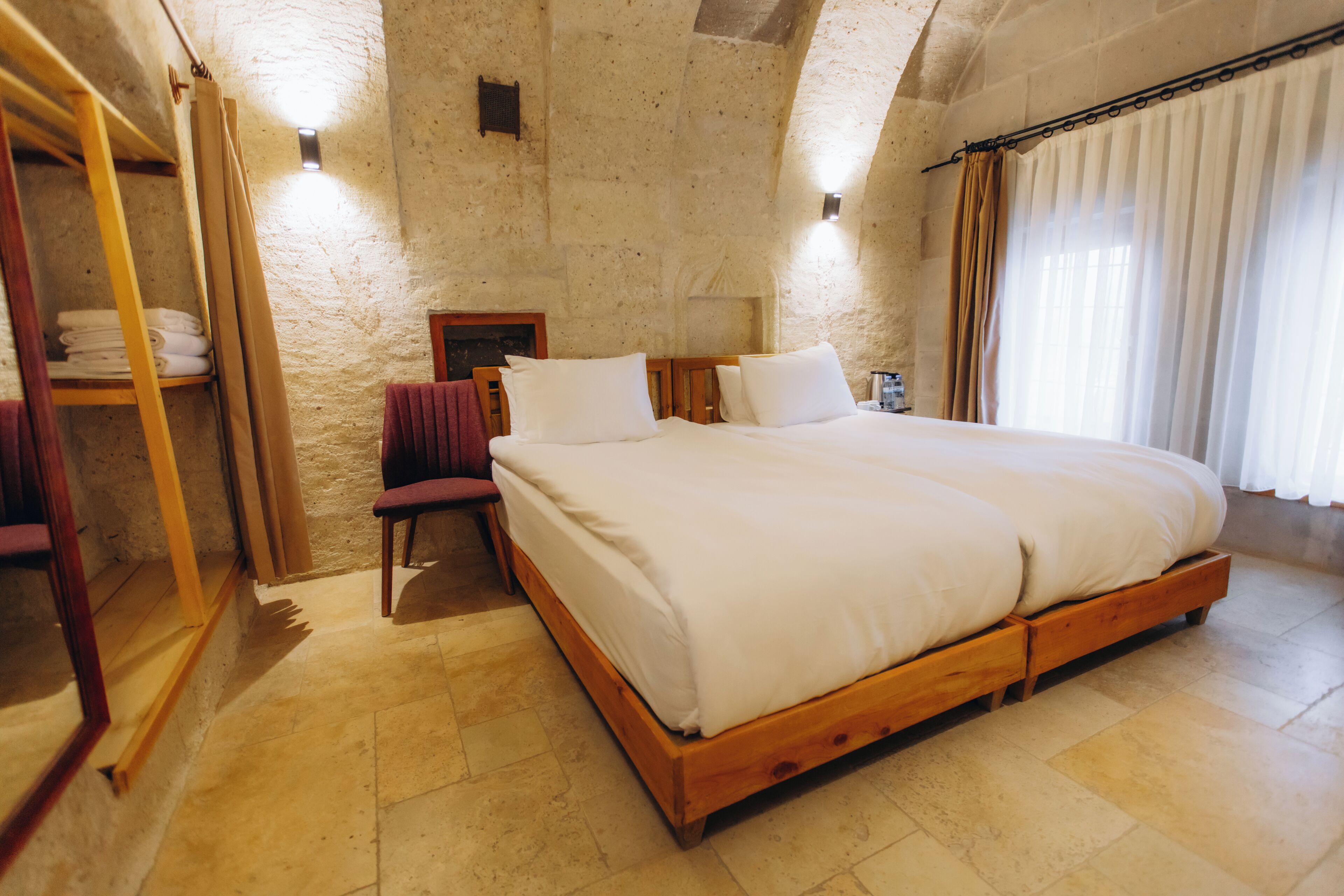 A bedroom with a large bed, wooden headboard, a wooden wardrobe, a chair, and a nightstand with a lamp.