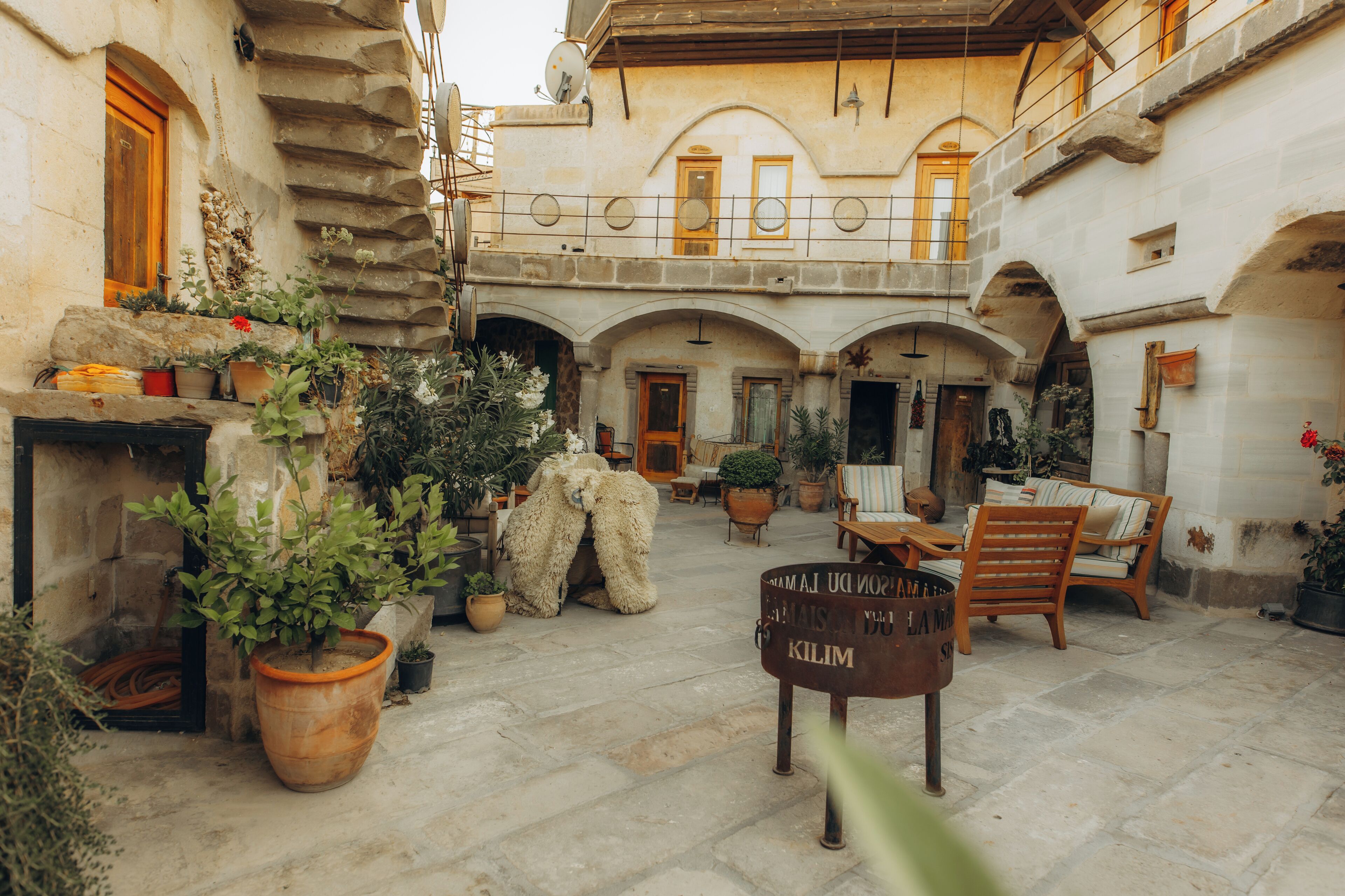 A courtyard with stone flooring, potted plants, outdoor furniture, and a sign with text.