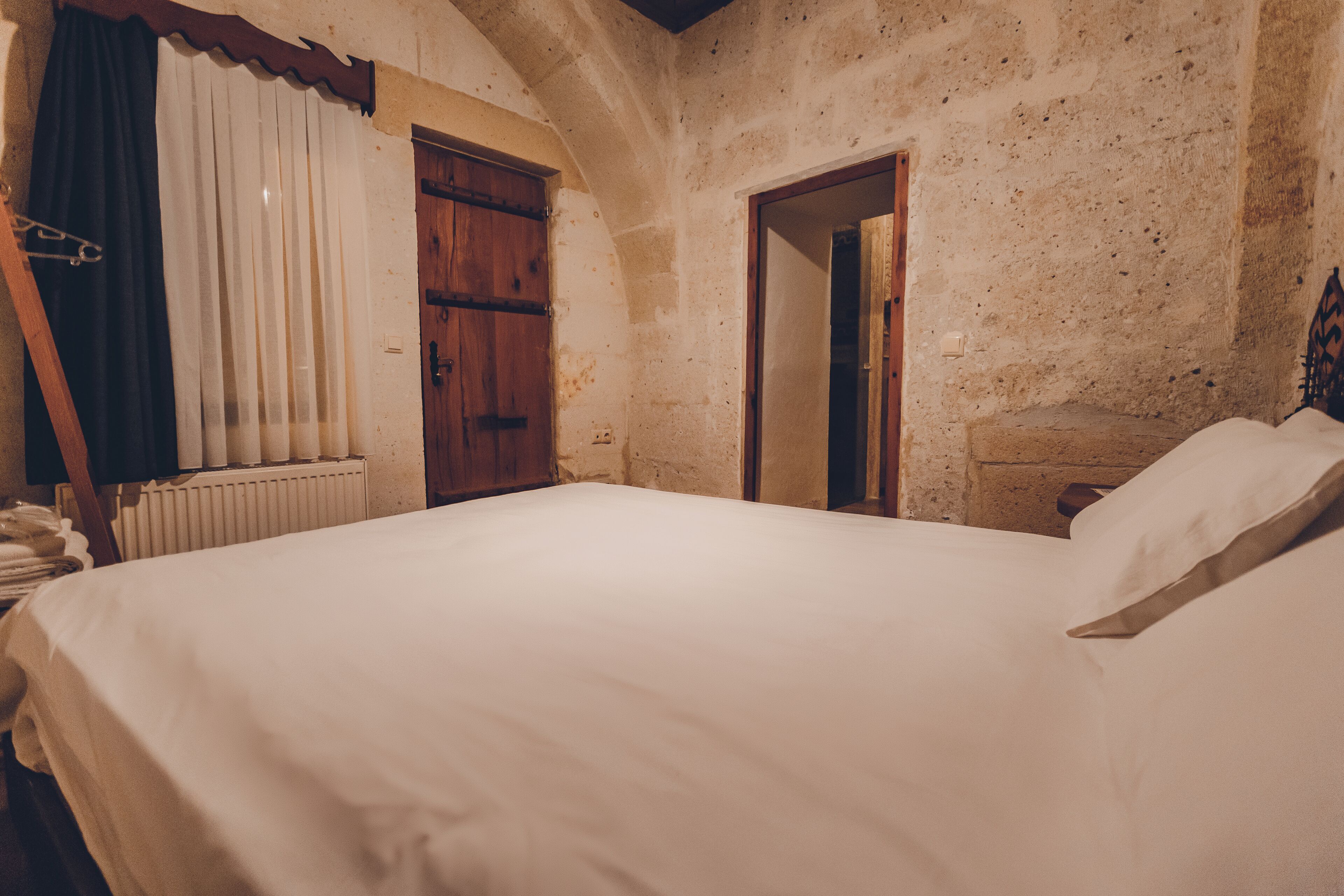 A bedroom with a large bed, a wooden wardrobe, a radiator, and a door leading to another room.