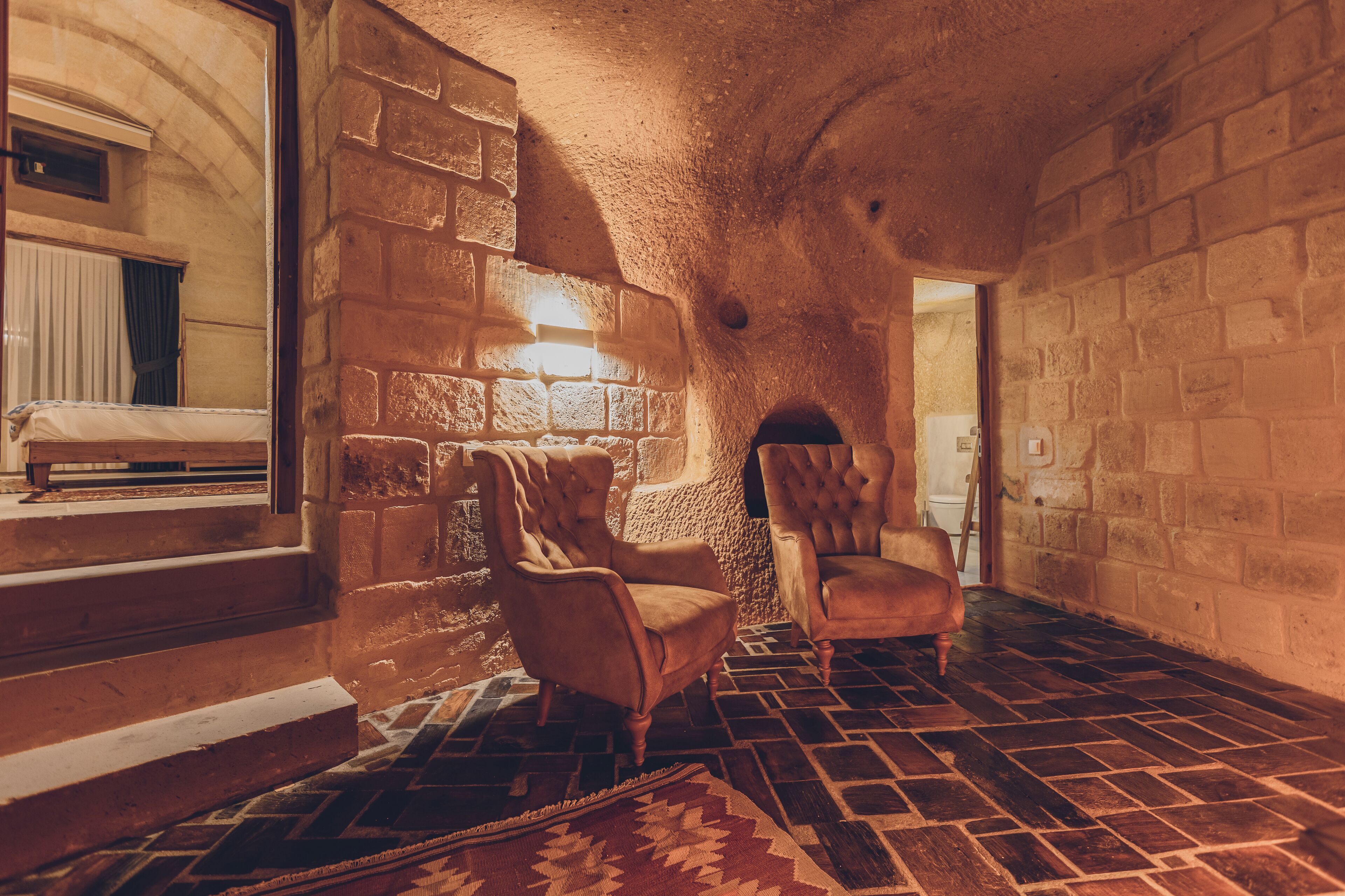 A room with stone walls, a patterned floor, and two upholstered chairs.