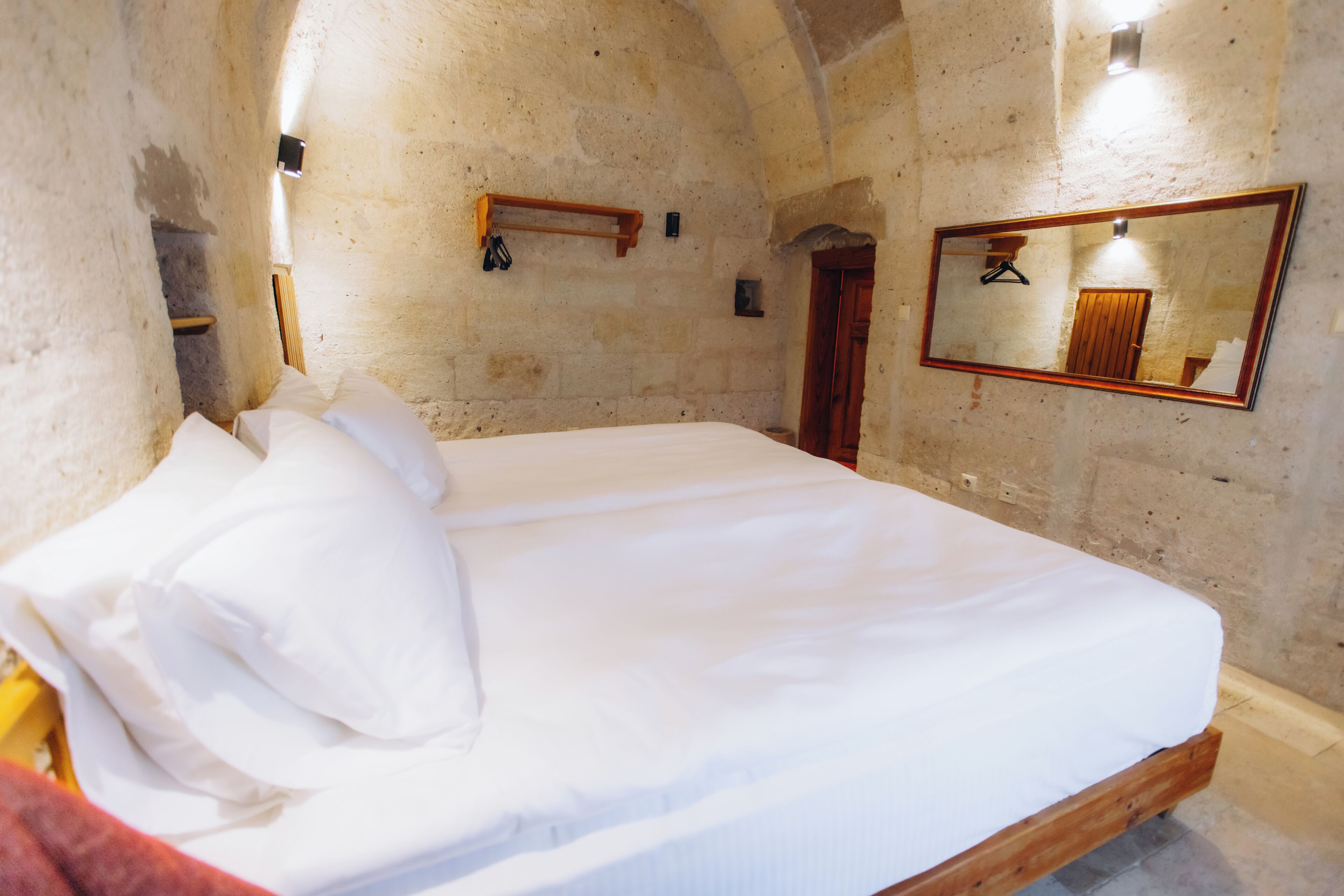 A bedroom with a bed, a wooden headboard, a mirror, and a stone wall.