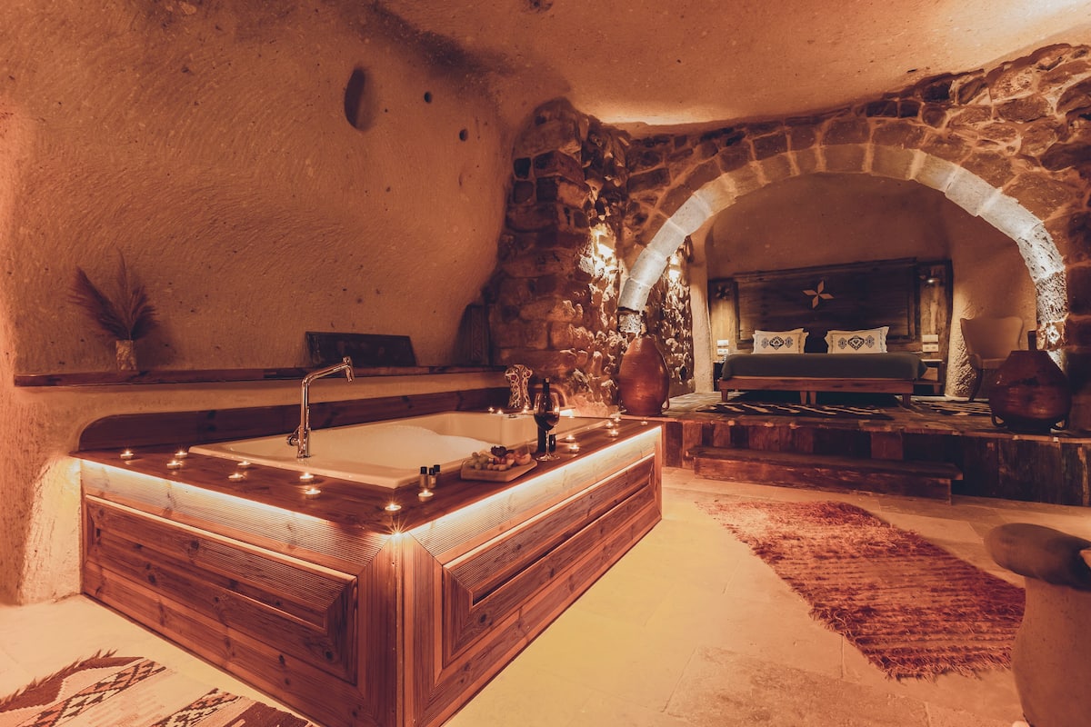 A stone-walled bathroom with a wooden vanity and a large bathtub.