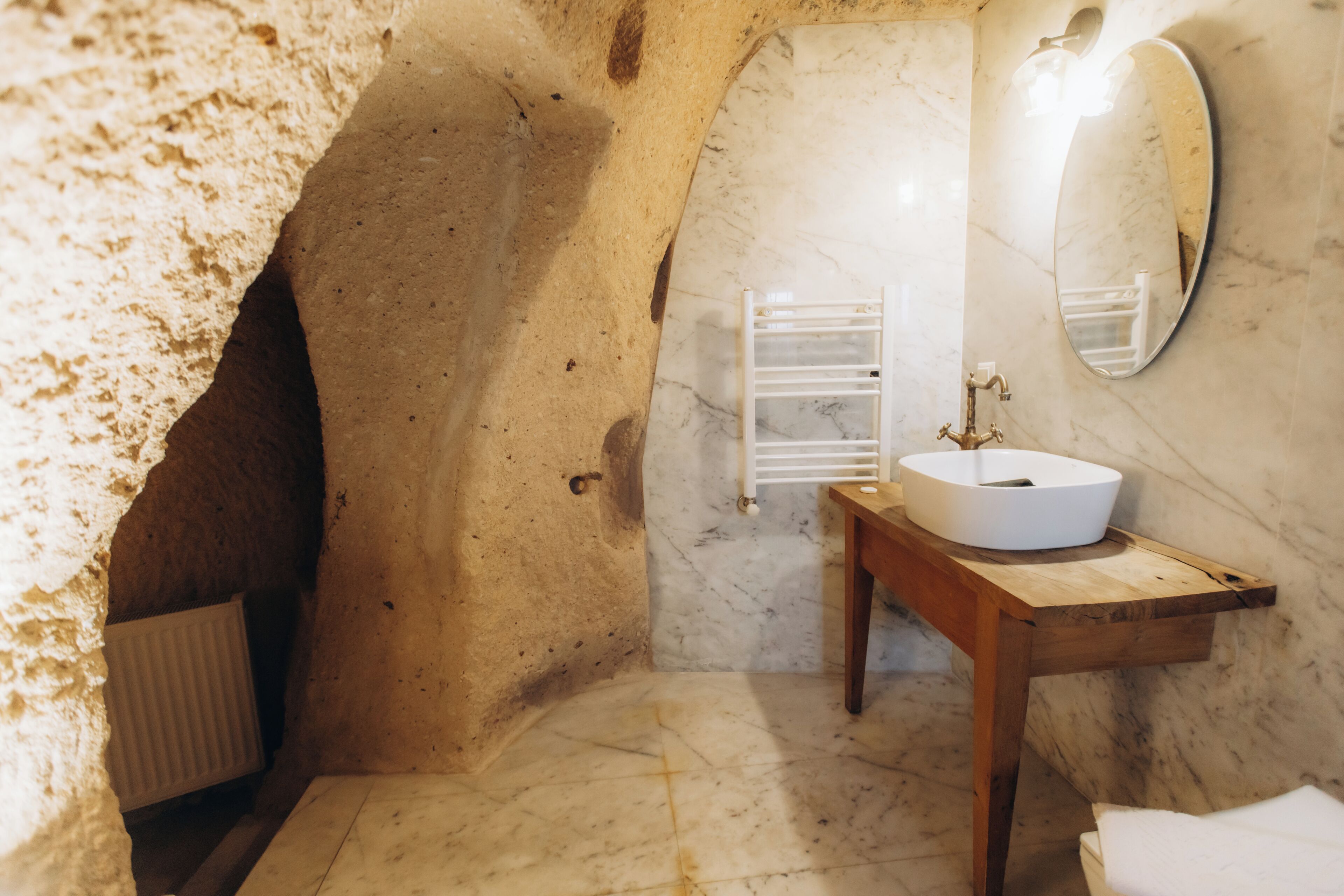 A bathroom with a marble sink, a wooden vanity, a mirror, and a towel rack.